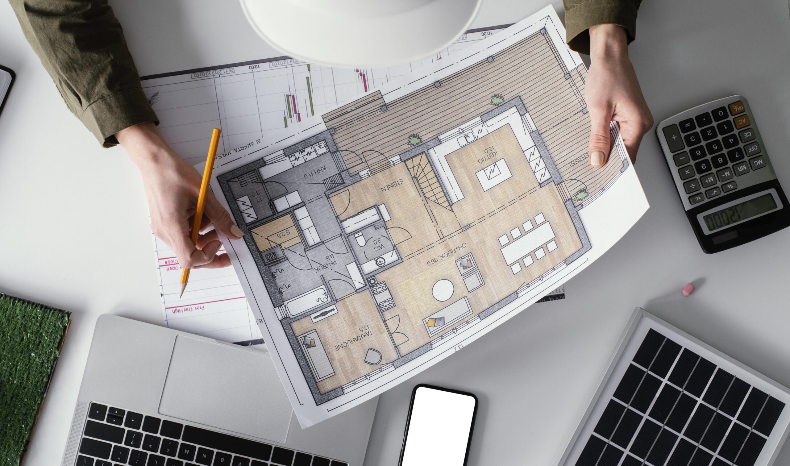 Architect reviewing granny flat designs Sydney floor plans with pencil, calculator and laptops on desk workspace